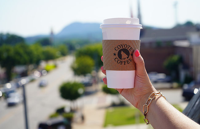 a hand holding a hot latte with the downtown pickens in the background