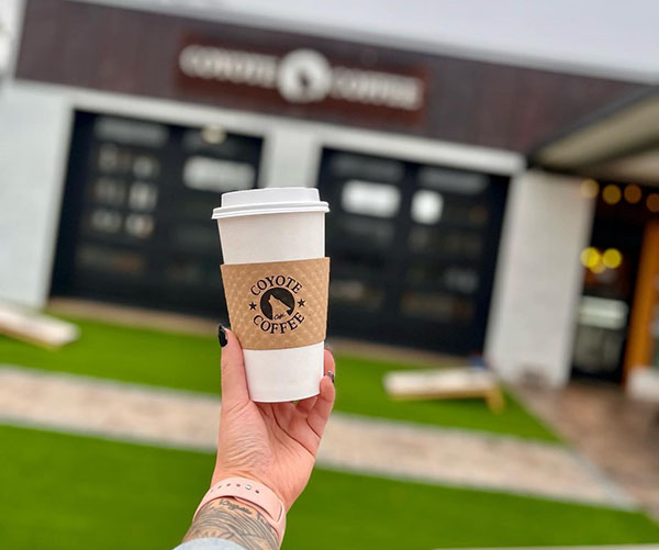 a hand holding a latte in front of the pickens coyote coffee